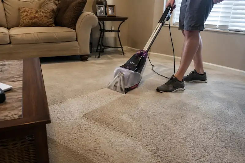 Person cleaning a carpet in a living room using a home carpet cleaner, showing a real-life DIY carpet cleaning process with visible carpet texture changes and natural indoor lighting.