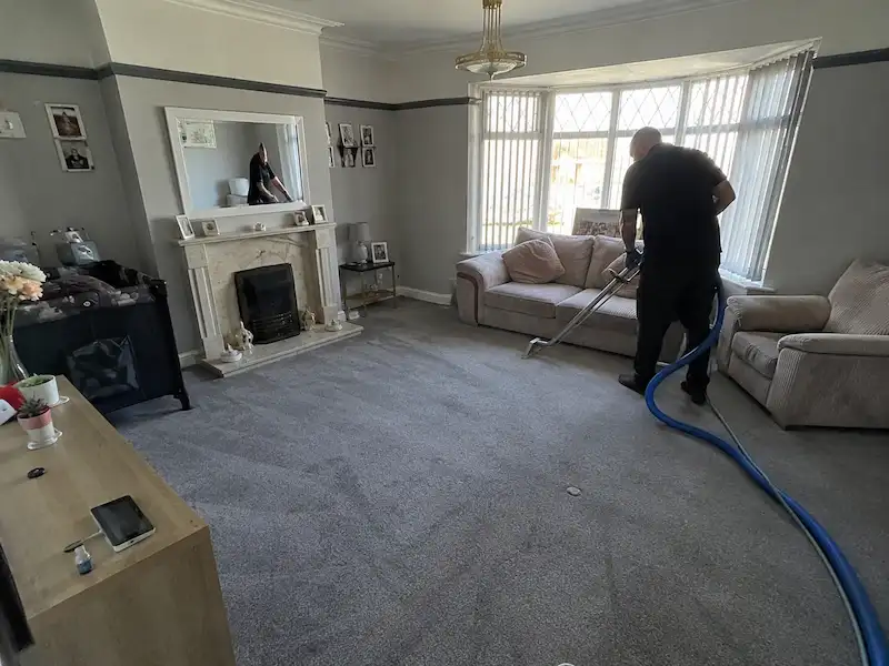 Wide view of a living room while a carpet cleaner deep cleans the grey carpet