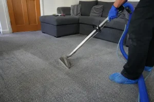 Professional carpet cleaner deep cleaning a grey living room carpet with a carpet extraction machine